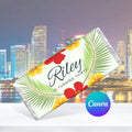 A tropical-themed birthday chocolate bar wrapper featuring palm leaves and hibiscus flowers, with the text 'Riley IS TURNING THIRTY!' and a Canva logo badge on a city skyline background.