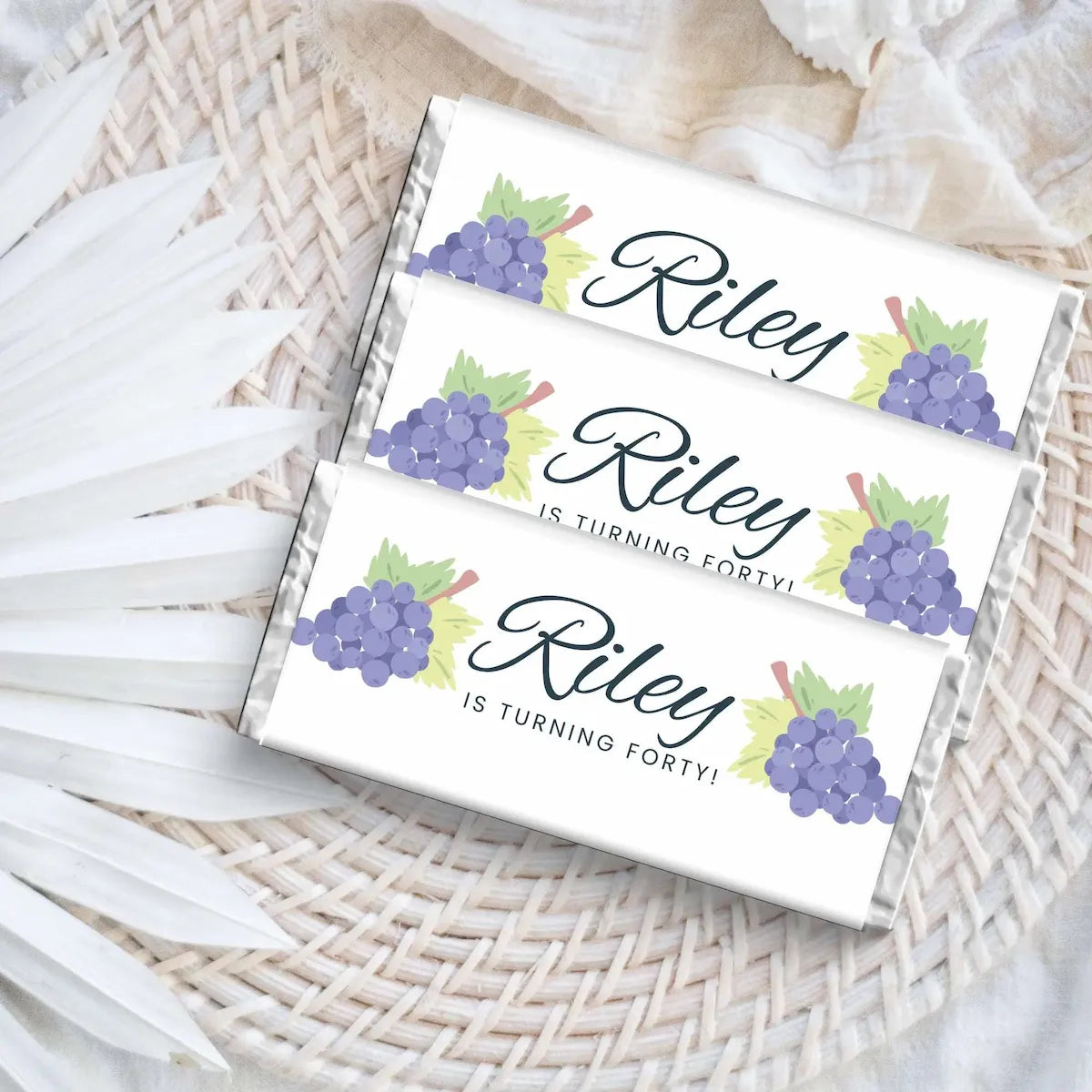 Three white boxes with purple grapes and Riley is turning 40 text on a woven surface