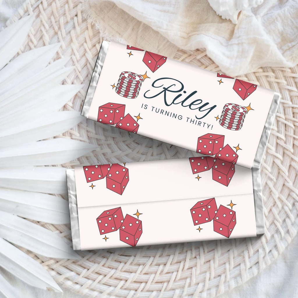 Two white chocolate bars with red dice illustrations and 'Riley is turning thirty!' text on a woven surface.