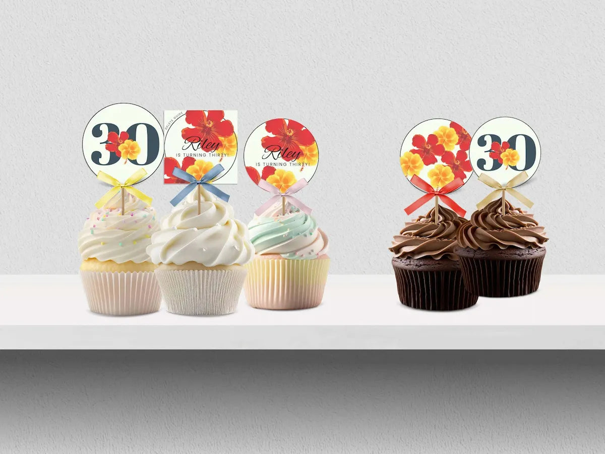 Two sets of tropical-themed cupcake toppers displayed on cupcakes. The left set features white and pastel frosted cupcakes with toppers showing a navy '30' with red and yellow flowers, a square card with 'Happy Birthday' and hibiscus flowers, and a round topper with red and yellow flowers.