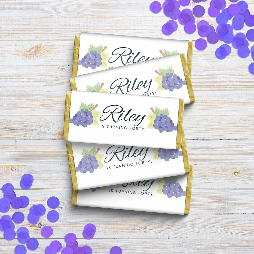 Personalized chocolate bars with 'Riley is turning forty!' text on a wooden surface with purple confetti.