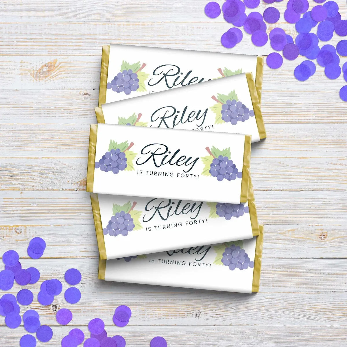 Personalized chocolate bars with 'Riley is turning forty!' text on a wooden surface with purple confetti.