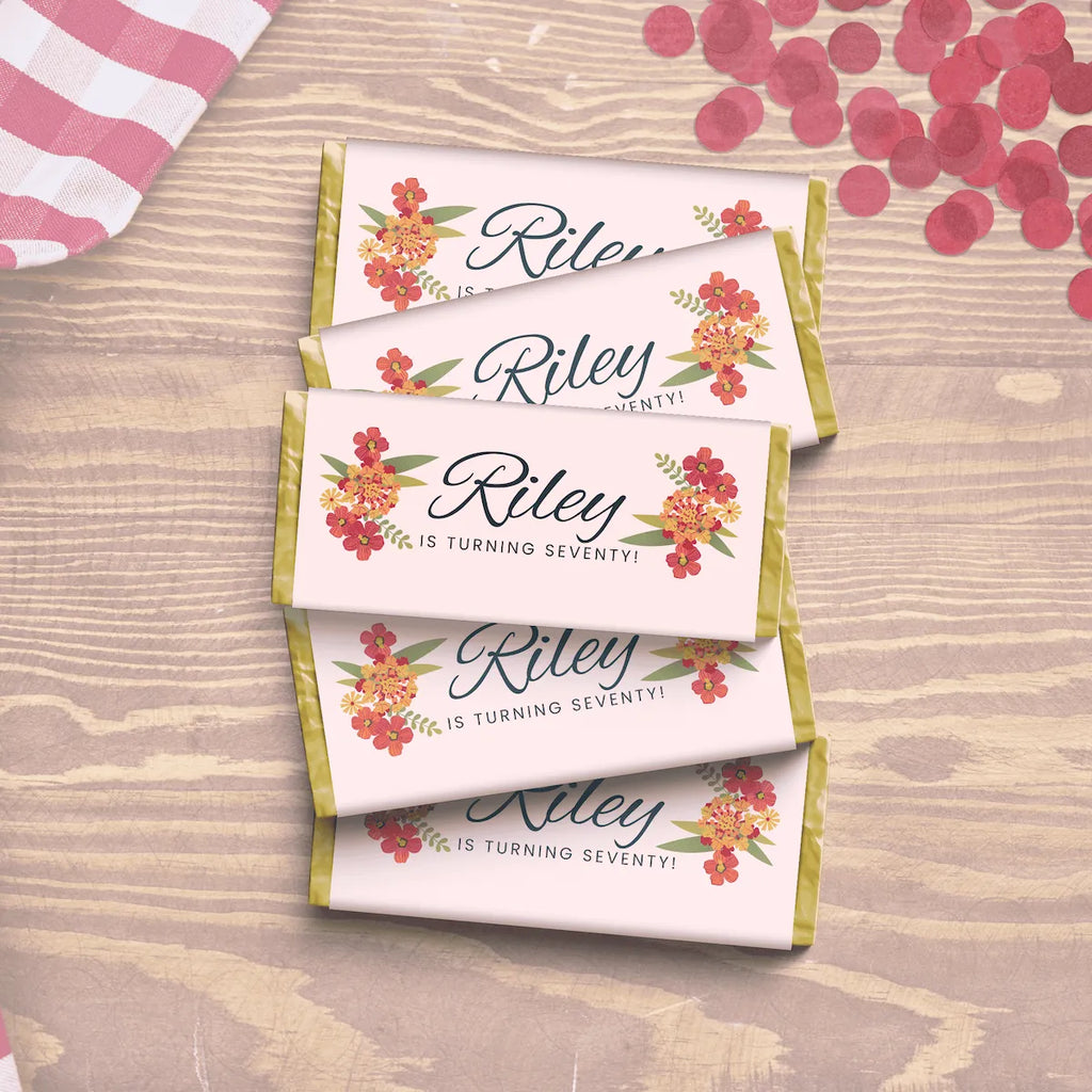 Personalized chocolate bars with floral designs and text Riley is turning seventy!on a wooden surface.