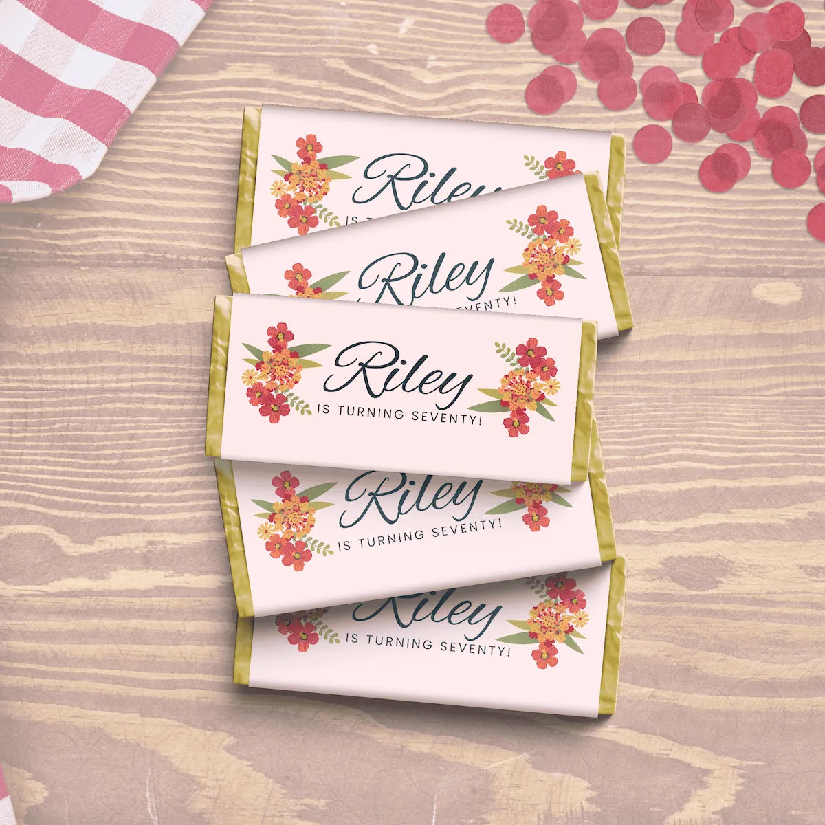 Personalized chocolate bars with floral designs and text Riley is turning seventy!on a wooden surface.