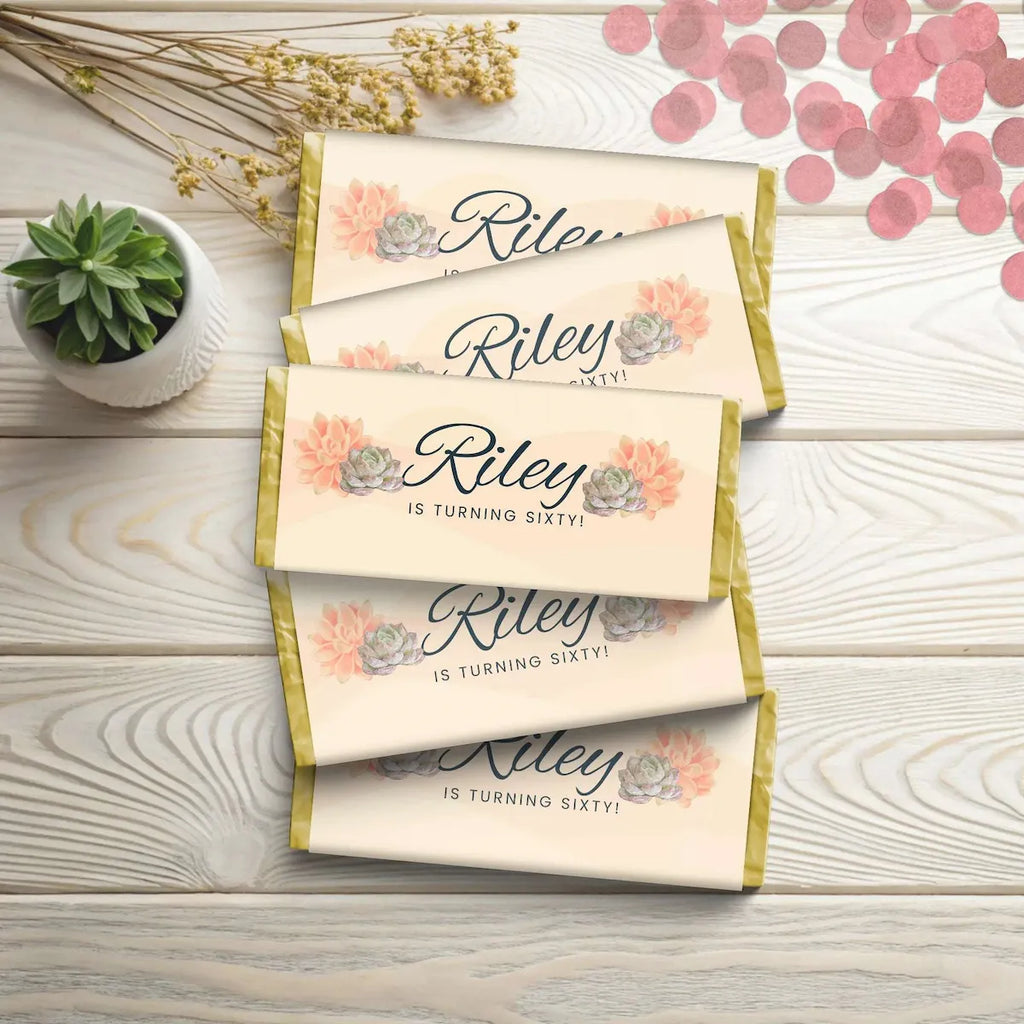 Personalized chocolate bars with 'Riley is turning sixty!' text on a wooden surface with decorative elements.