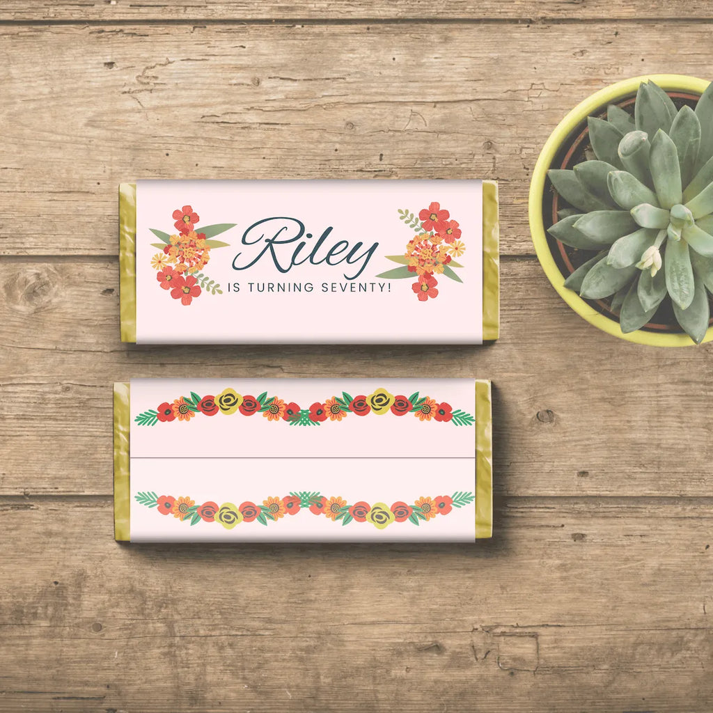 Candy bars with floral designs and text Riley is turning seventy! on a wooden surface with a potted plant.