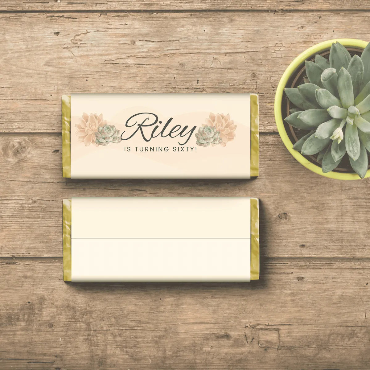 Two candy bars with text Riley is turning fifty on one side with floral designs and a back of candy bar blank on a wooden surface, accompanied by a small potted plant. 
