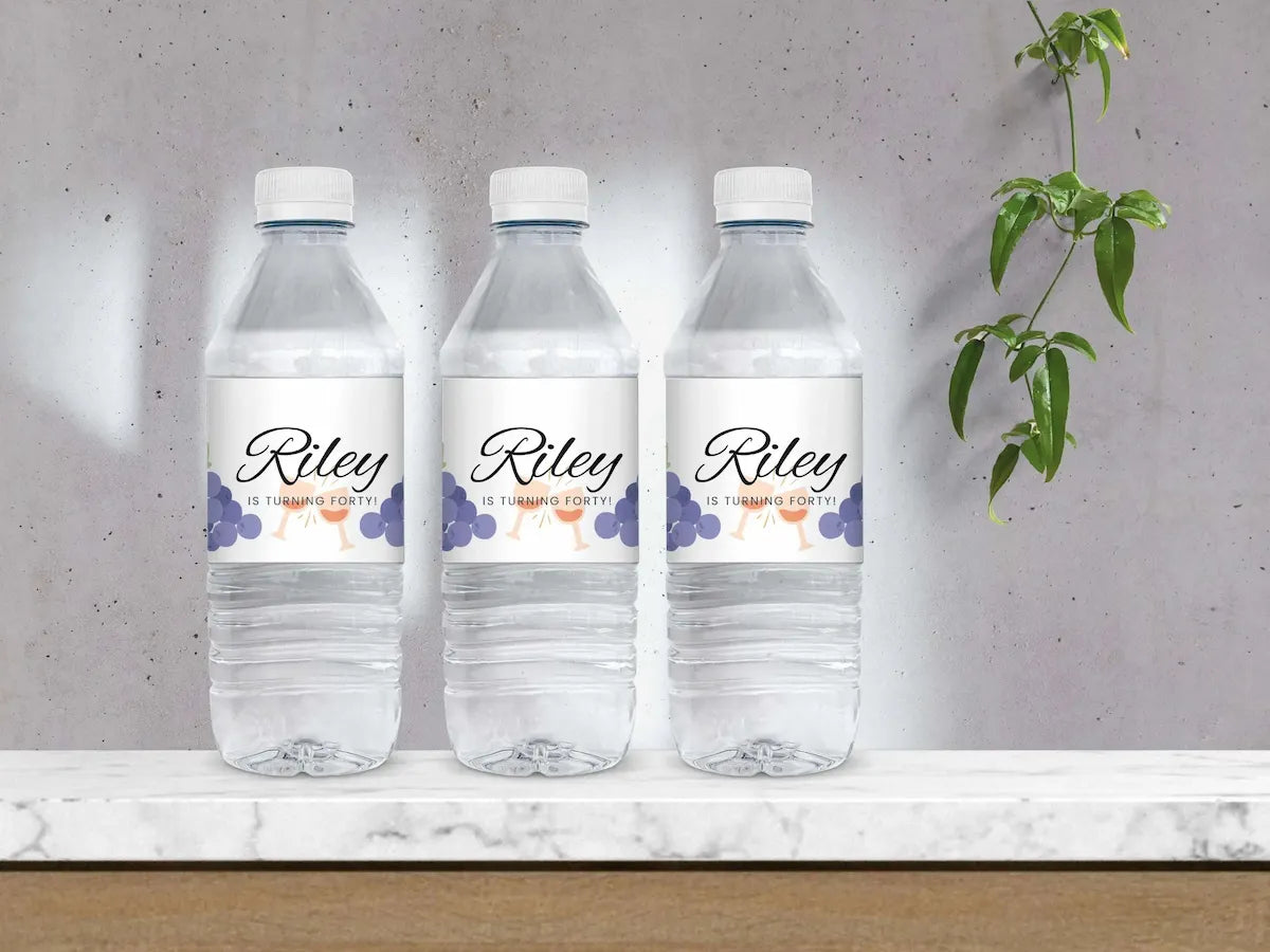 Three 'Riley' is turning forty! water bottles with labels on a marble surface against a gray wall.