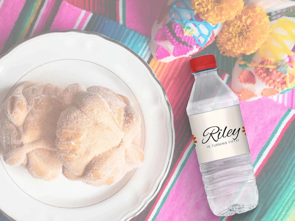 Bottle of Riley is turning 50 water next to a plate of food on a colorful tablecloth.
